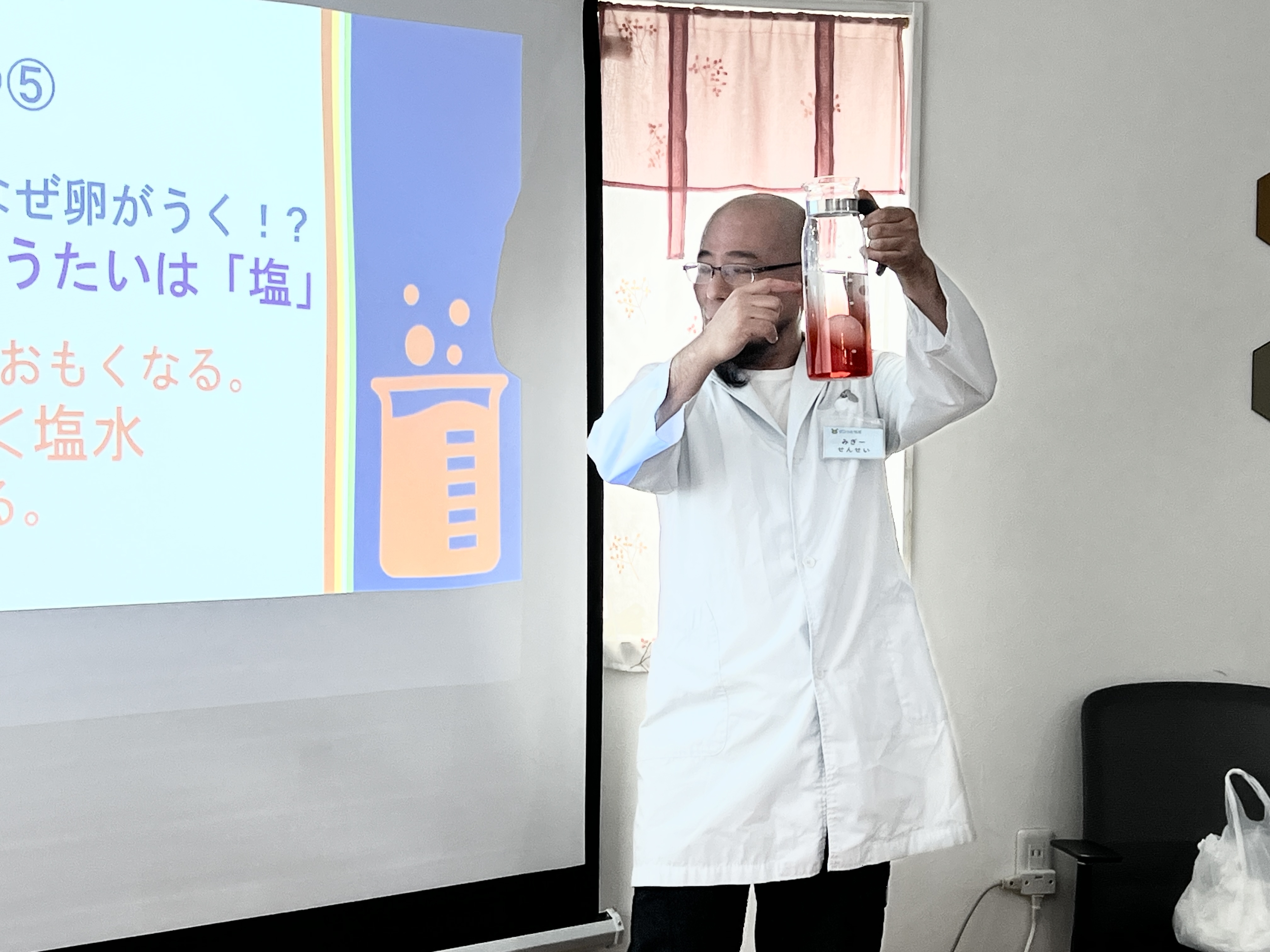 塩水を高くかかげ「まほうの粉のしょうたいは塩！」と解説する白衣姿のミギー先生